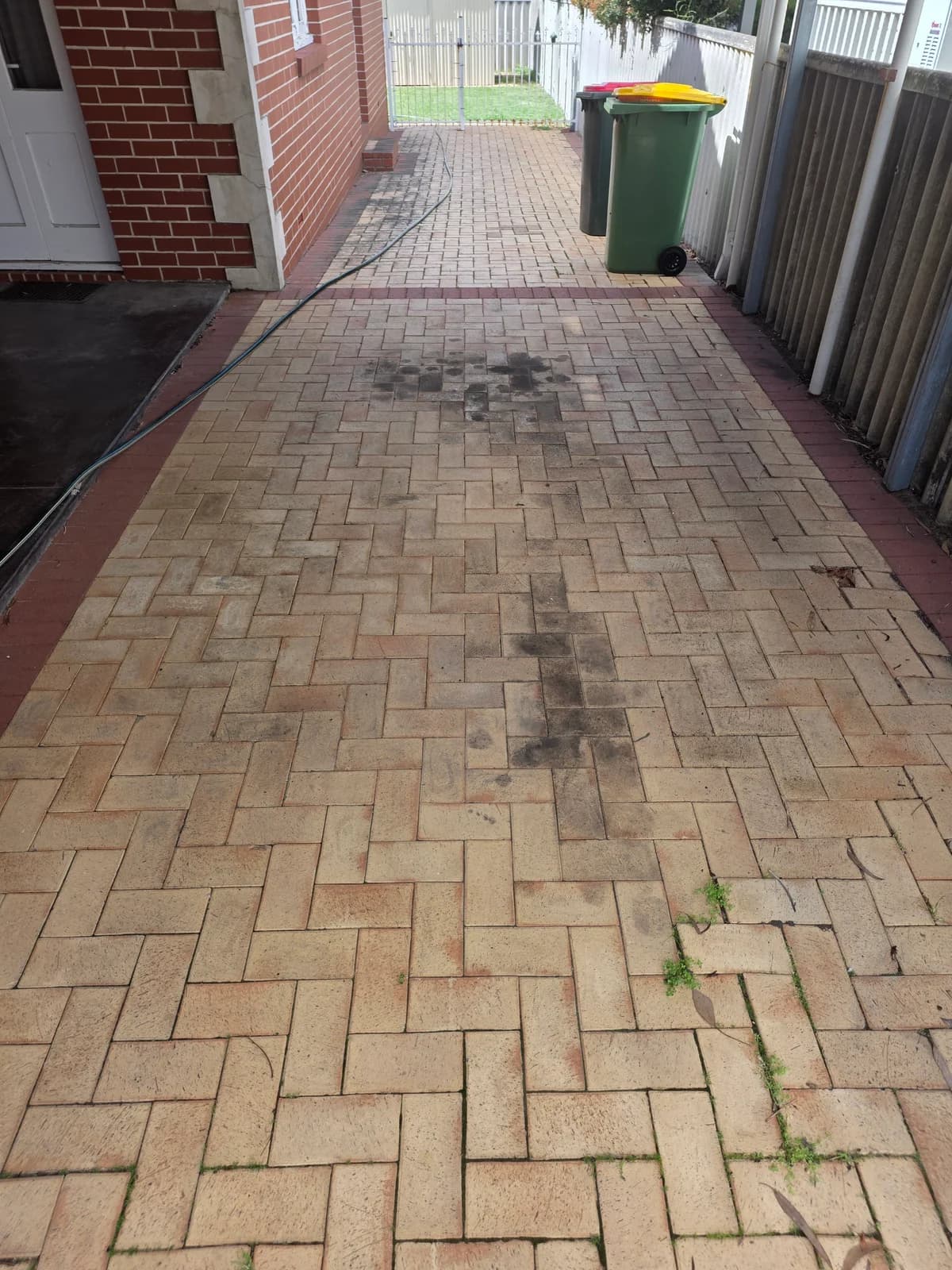 Carport pavers before pressure cleaning, with dark marks and built-up grime across the centre and joints.
