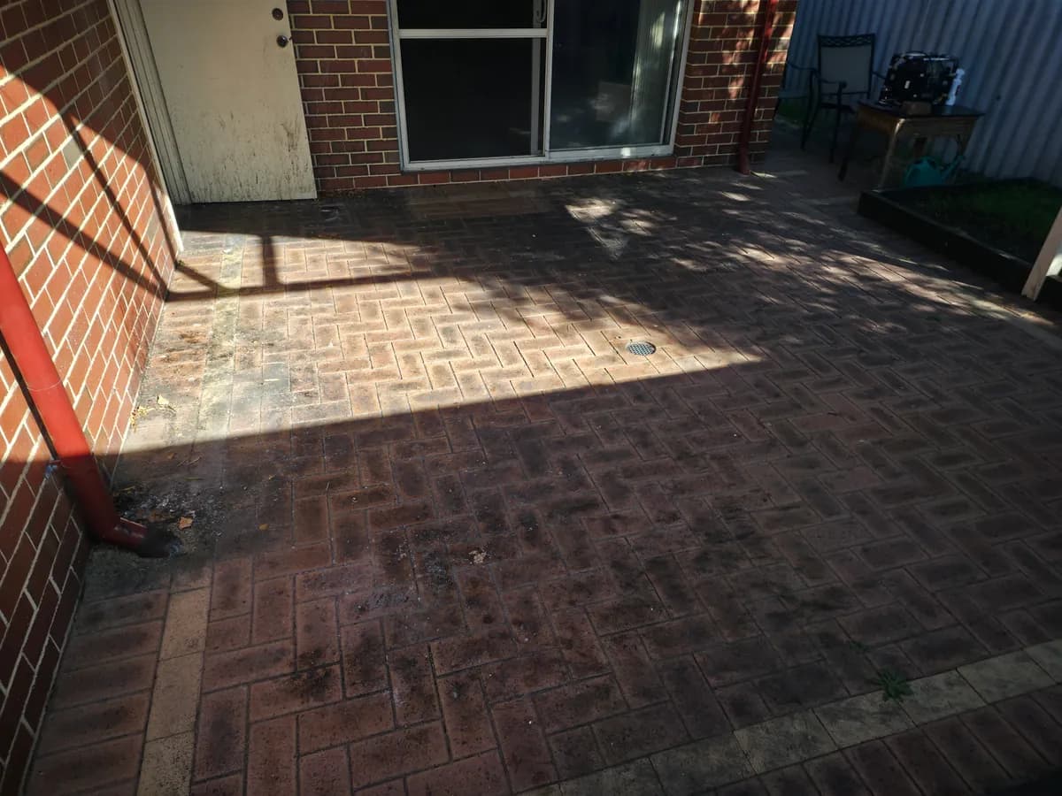 Paved courtyard before AGP pressure cleaning, with dark traffic marks and built-up grime.